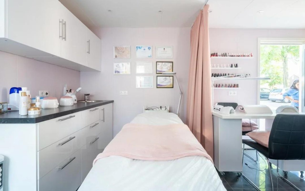 Behandelbed met roze plaid, witte kasten en certificaten aan de wand
